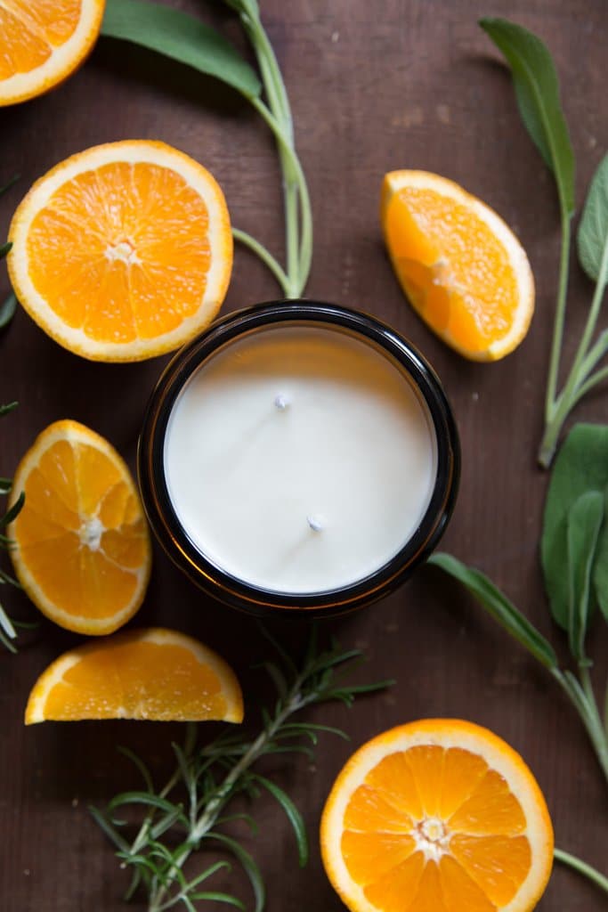 Open jar of Italian Garden candle surrounded by cut oranges and sprigs.